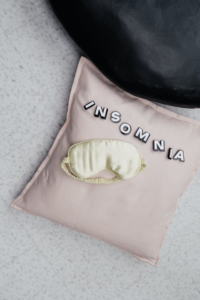 A sleep mask lying on a pillow reading insomnia